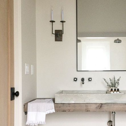Concrete sink basin over a wood slab counter, light wood door with clean black hardware, old school sink faucets, candle sconces featured here in the home as well, this lighting choice brings a pre-electricity, old school vibe to the home which takes you back to the simpler times. (Photography by Alyssa Rosenheck)