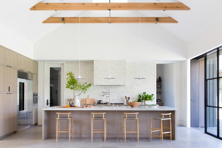 A large kitchen with loads of natural light greets you upon entering the home. Its sky-high vaulted ceiling is adorned with large exposed beams from which a trio of sleek pendants are hung.