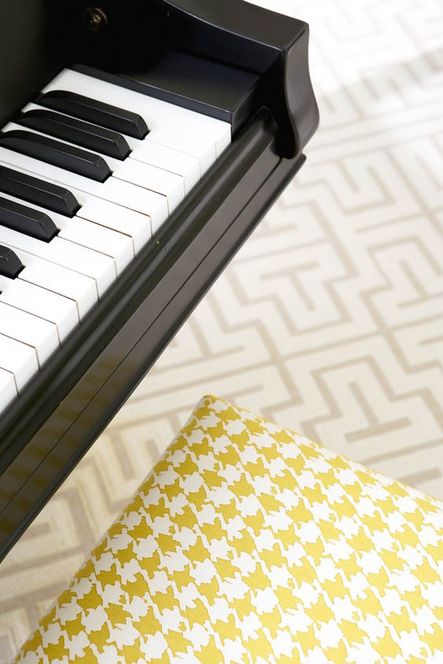 A yellow herringbone piano bench contrasts grey geometric flooring.