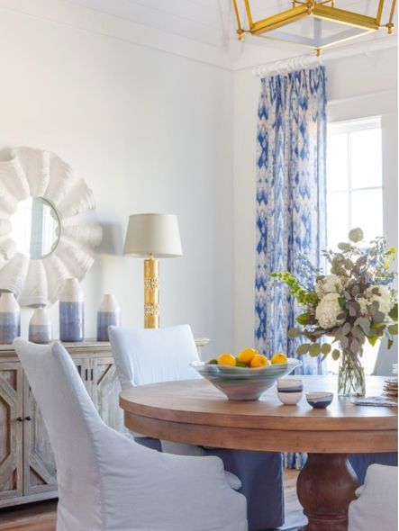 A round wooden dining table centering the space is styled with a bowl of fruit and florals.