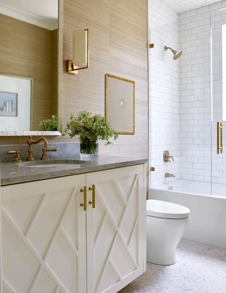 A geometric-front cabinet with brass pulls creates bathroom storage and adds visual interest to the space. Square framed art featured in this space soften the walls, and a window in the shower brings in loads of natural light.