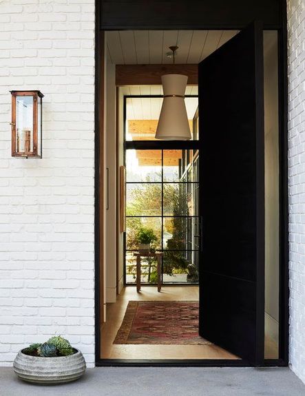 The dark-toned front door is beautifully contrasted by the exterior of the home, which practically begs you to enter. The white lighting fixture placed in the entryway paired with the vintage rug create an inviting environment, while also drawing the eyes to the view out of the full-length windows.